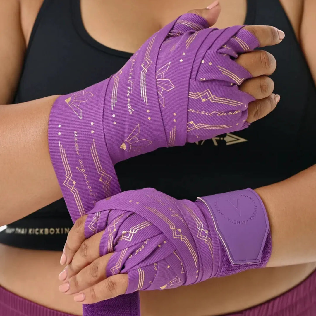Close-up van het wikkelproces van de paarse Athena Fightwear handwraps. De gouden accenten vallen duidelijk op tegen de paarse achtergrond. De foto toont hoe strak en ondersteunend de wraps om de handen kunnen worden aangebracht.