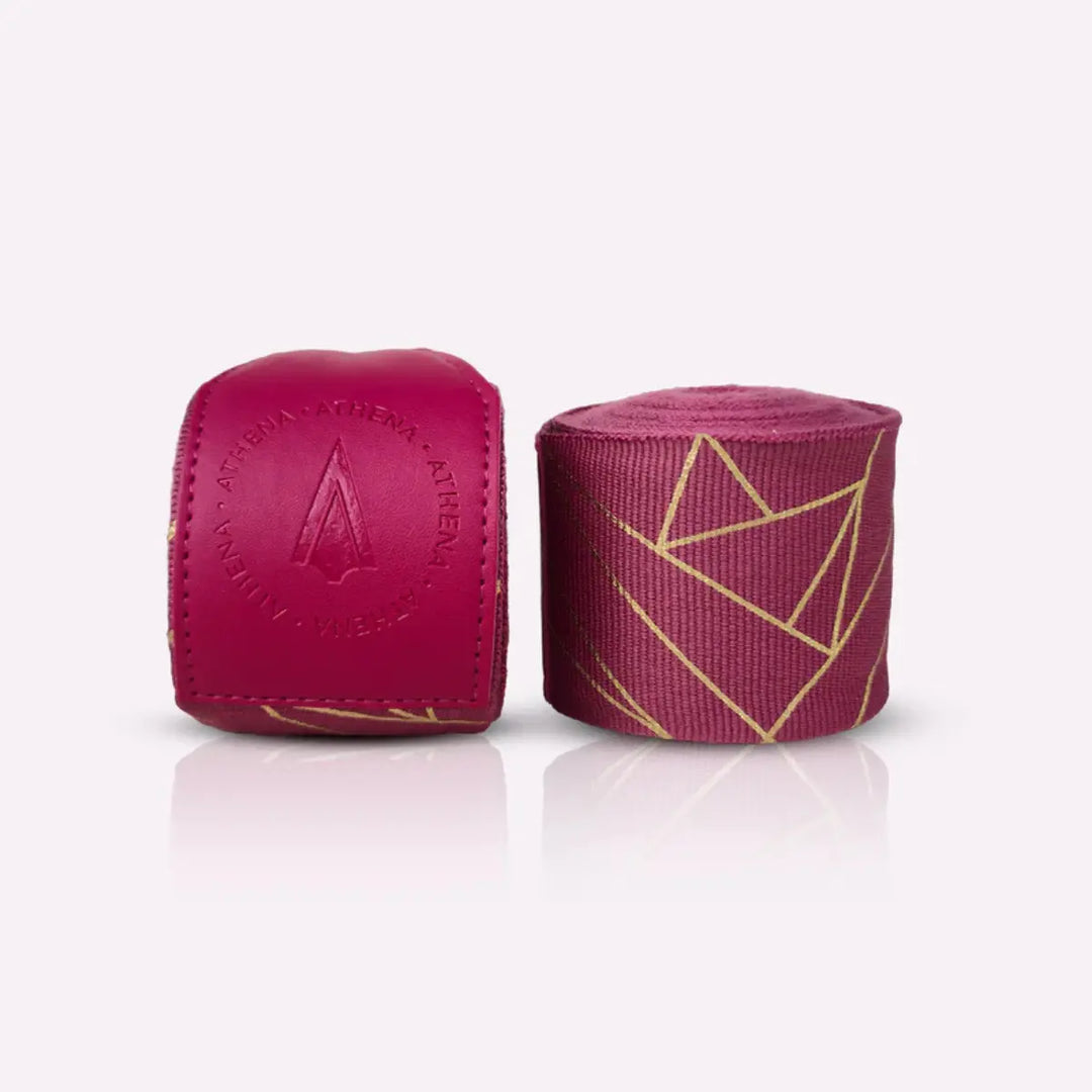 Athena Fightwear Eris Berry handwraps in opgerolde vorm naast de stevige polssluiting. De gouden geometrische lijnen geven de bandages een luxe uitstraling. De foto toont de structuur en kwaliteit van het materiaal duidelijk.
