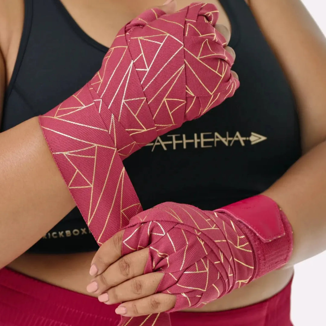 Close-up van een model dat de Eris Berry handwraps strak om de handen wikkelt. De gouden lijnen komen mooi naar voren tegen de diepe berry-kleur. De foto laat zien hoe ondersteunend en stevig de wraps zitten.
