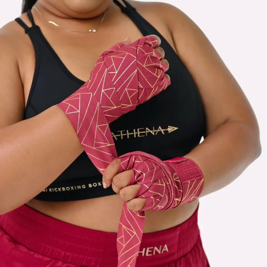 Model draagt de Eris Berry handwraps tijdens het wikkelproces. De gouden patronen en de diepe kleur geven de wraps een opvallende en stijlvolle uitstraling. De pasvorm toont hoe goed ze aansluiten bij bokstraining.