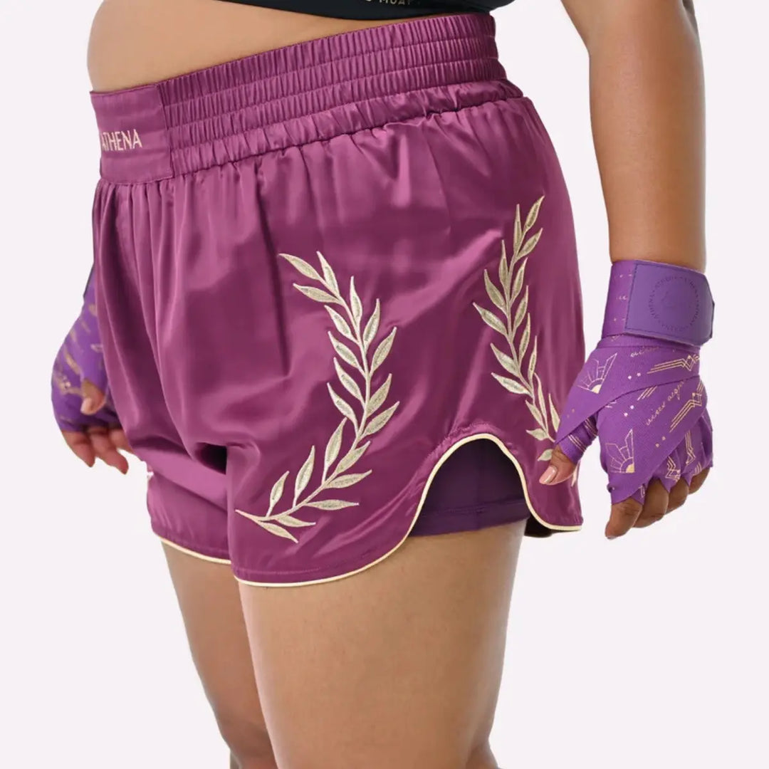 Vrouw draagt het Athena Fightwear Thaiboks Broekje in plum met gouden lauwerdetails tijdens een training.