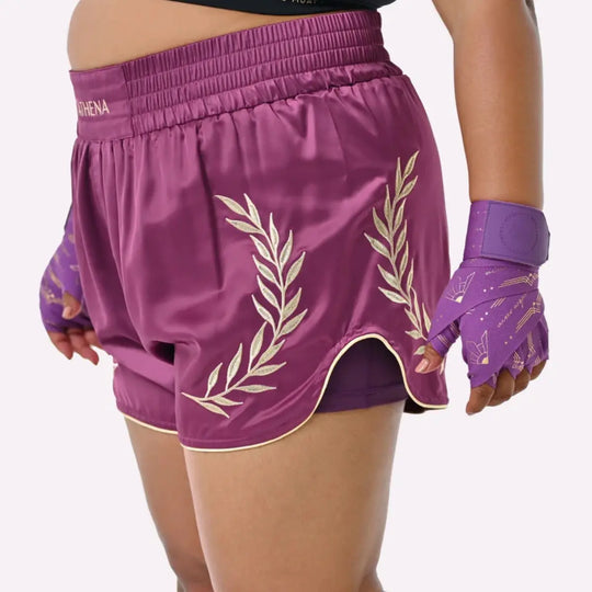 Vrouw draagt het Athena Fightwear Thaiboks Broekje in plum met gouden lauwerdetails tijdens een training.