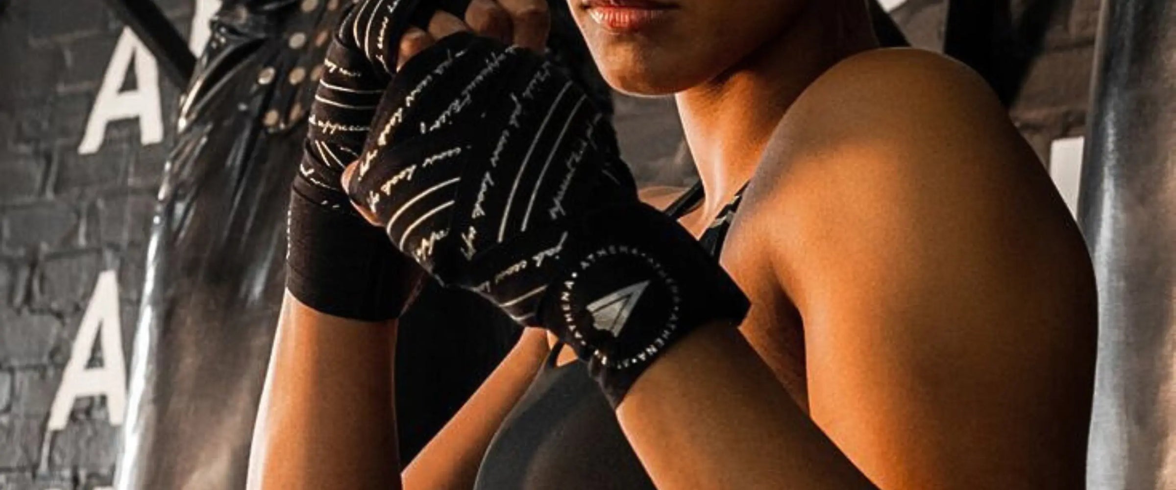 Vrouwelijke sporter in de gym met Athena Fightwear handwraps in zwart, zichtbaar tijdens training bij de bokszak met focus op grip en ondersteuning.