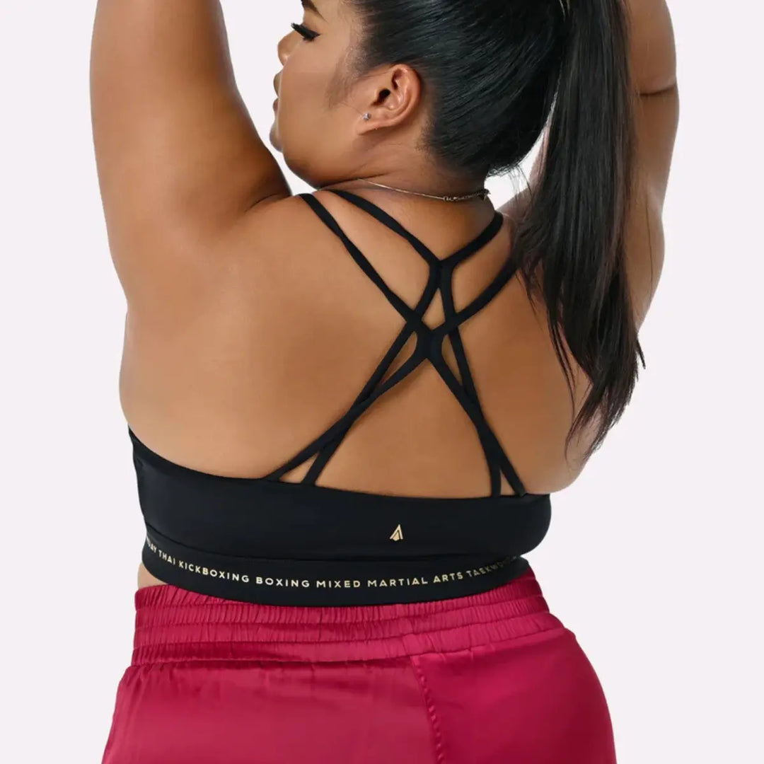 De afbeelding toont de achterkant van de zwarte Thessalia sport-BH van Athena Fightwear, met meerdere elegante gekruiste bandjes en een stevige elastische band onder de borst, gedragen door een vrouwelijke atlete.