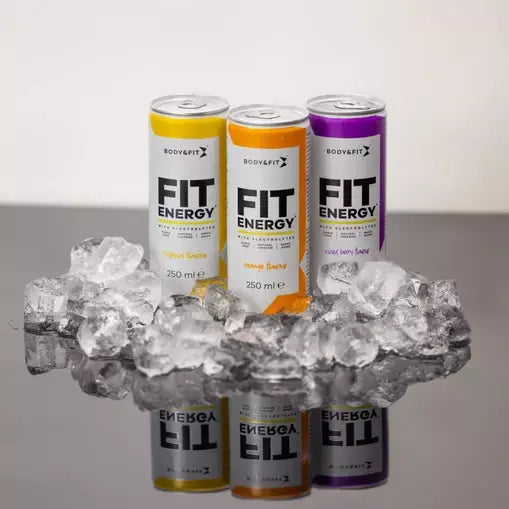 Drie blikjes Body & Fit Fit Energy Drink in de smaken Tropical, Orange en Mixed Berry, gepresenteerd op een spiegelend oppervlak omringd door ijsblokjes.