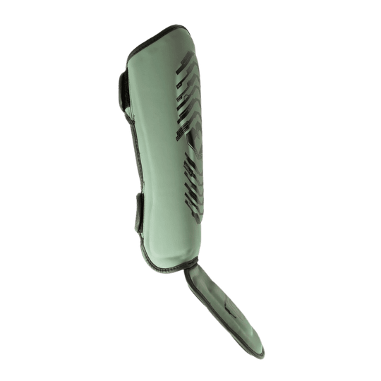 Zijaanzicht van een groene Booster scheenbeschermer met zwart design, duidelijk zichtbare voetbescherming en klittenbandsluiting aan de achterzijde.