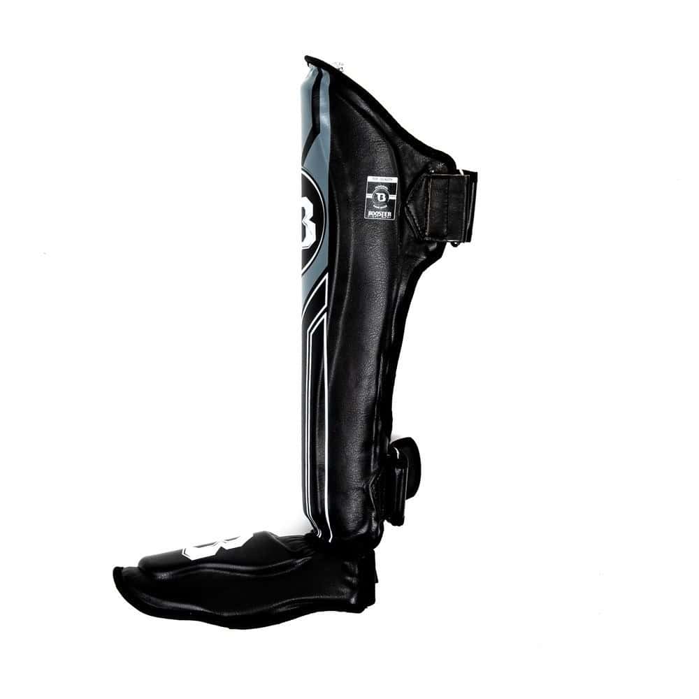 Zijaanzicht van de Booster Scheenbeschermers BSG V9 in zwart met grijze afwerking, met dubbele klittenbandsluiting voor optimale pasvorm en stabiliteit tijdens intensieve kickbokstrainingen.