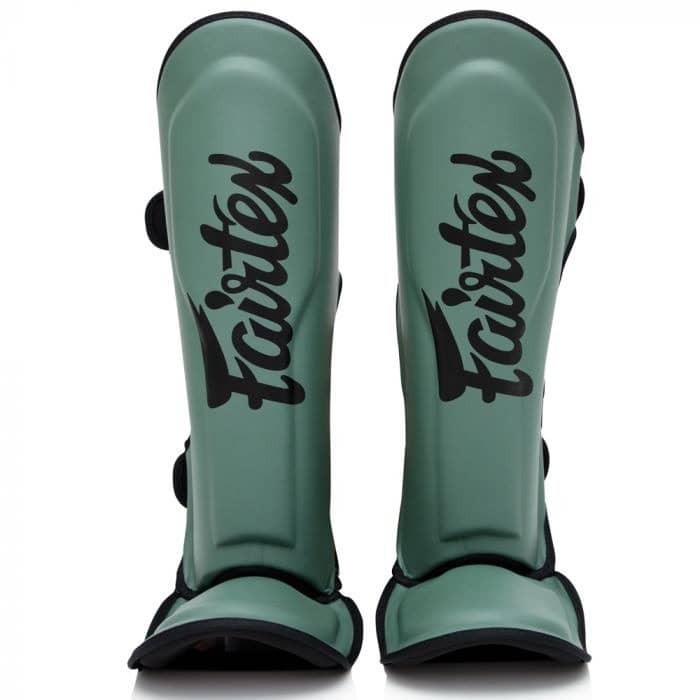 Fairtex scheenbeschermers in matte groene kleur met zwart logo, rechtopstaand weergegeven tegen een witte achtergrond. De padding is anatomisch gevormd en voorzien van klittenbandsluitingen aan de achterkant voor stevige pasvorm tijdens kickbokstrainingen.