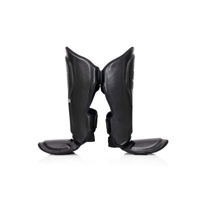 Zwarte Fairtex scheenbeschermers van de zijkant gefotografeerd, met duidelijke zichtbaarheid van de anatomisch gevormde padding en stevige enkelbescherming. Ontworpen voor optimale pasvorm en bewegingsvrijheid tijdens kickbokstraining.