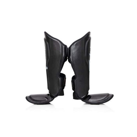 Zwarte Fairtex scheenbeschermers van de zijkant gefotografeerd, met duidelijke zichtbaarheid van de anatomisch gevormde padding en stevige enkelbescherming. Ontworpen voor optimale pasvorm en bewegingsvrijheid tijdens kickbokstraining.