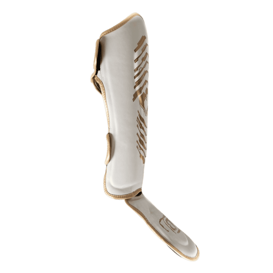 Zijaanzicht van een witte Booster scheenbeschermer met gouden design, voorzien van voetbescherming en klittenbandsluiting voor een stevige pasvorm
