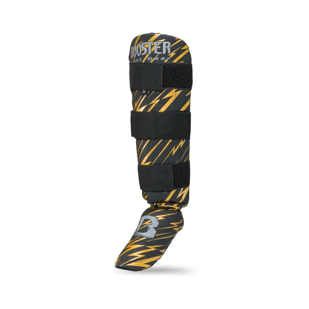 Schuin-vooraanzicht van de Booster Combat Series Youth scheenbeschermer met goudkleurig bliksemdesign, zwarte klittenbandsluitingen en grijs Booster-logo op de wreef.









