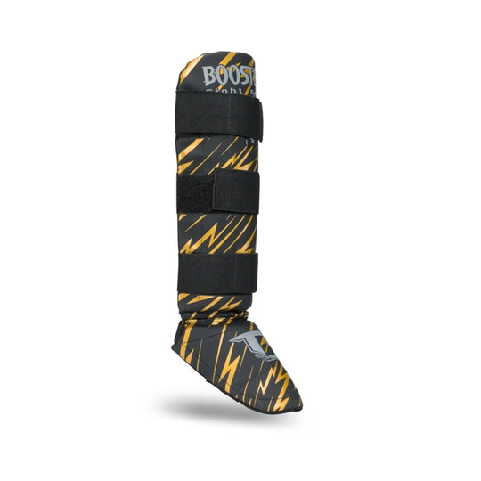 Zijaanzicht van de Booster Combat Series Youth scheenbeschermer in zwart met gouden bliksemschichtdesign en stevige klittenbandsluitingen voor optimale pasvorm.









