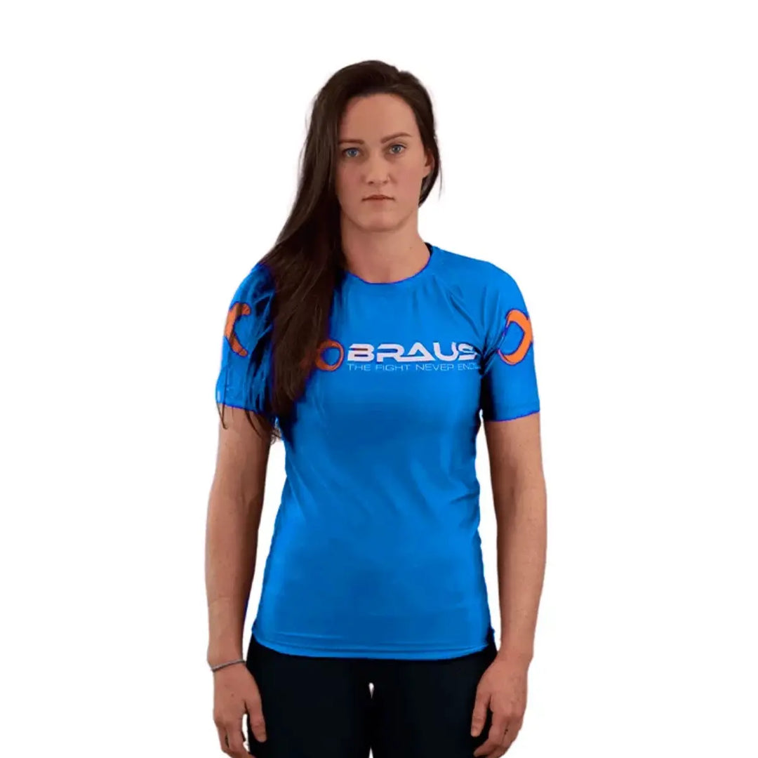 Vrouw draagt blauwe Braus rashguard met korte mouwen, wit logo op de borst en oranje accenten op de mouwen.