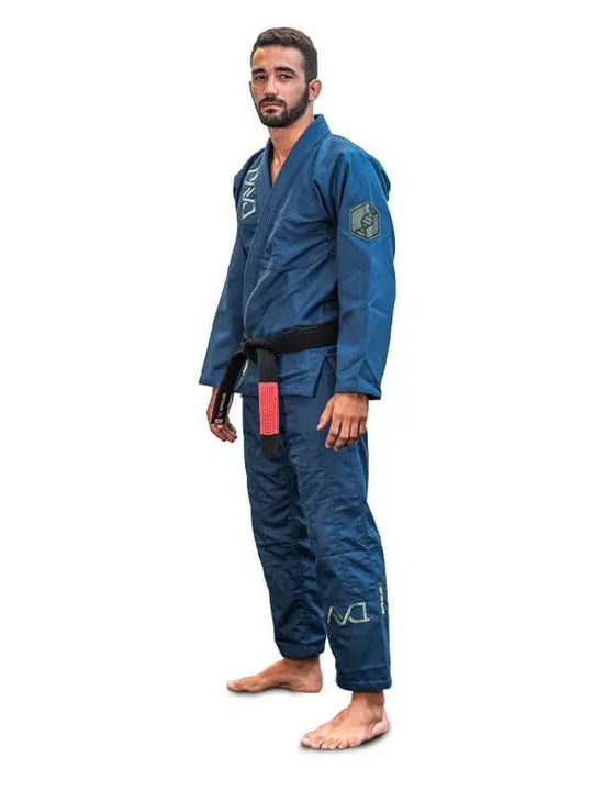 Man in blauwe BJJ-gi met zwarte band staat rechtop in ontspannen houding op een witte achtergrond.