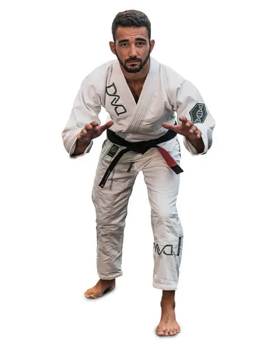 Man in een witte BJJ-gi met zwarte band staat in lage vechthouding op een witte achtergrond.
