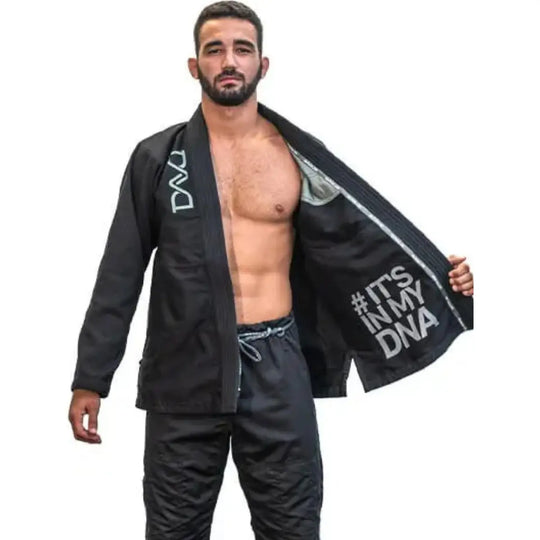 Man poseert met opengeklapte zwarte Brazilian Jiu-Jitsu gi waarin de binnenzijde bedrukt is met de tekst ‘#It’s in my DNA’.









