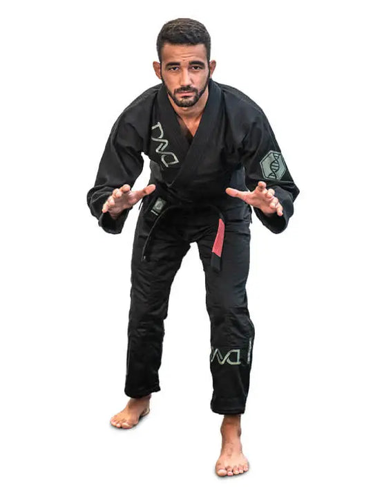 Man in zwarte BJJ-gi met zwarte band staat in een lage vechthouding, klaar voor actie op een witte achtergrond.