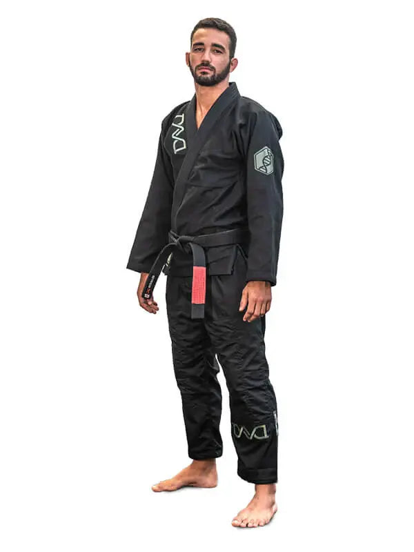 Man in zwarte BJJ-gi met zwarte band staat rechtop in ontspannen houding op een witte achtergrond.