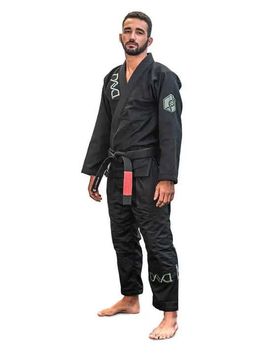 Man in zwarte BJJ-gi met zwarte band staat rechtop in ontspannen houding op een witte achtergrond.
