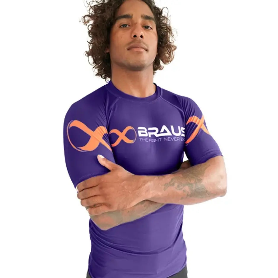 Man draagt een paarse Braus rashguard met korte mouwen en oranje logo, ontworpen voor comfort en prestaties tijdens bokstraining.