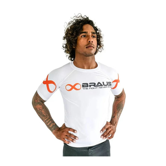 Man poseert in witte Braus rashguard met korte mouwen, zwarte tekst en oranje logo’s, ideaal voor kickboksen en boksen.
