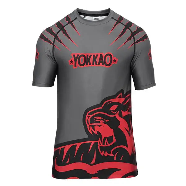 Vooraanzicht van het Yokkao compression shirt in grijs met rood en zwart design. Het shirt heeft een opvallende tijgerprint aan de onderzijde en rode kraslijnen op de schouders, met het Yokkao-logo op de borst. De strakke pasvorm en korte mouwen zorgen voor optimale ondersteuning en bewegingsvrijheid tijdens intensieve trainingen.