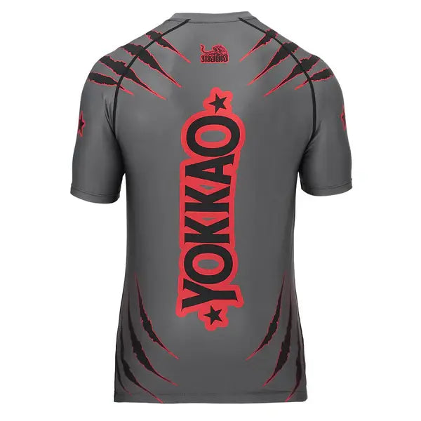 Achteraanzicht van het Yokkao compression shirt in grijs met rood en zwart design. Op de rug staat een groot verticaal Yokkao-logo in rood met zwarte omlijning, gecombineerd met rode krasdetails. De nauwsluitende pasvorm en korte mouwen bieden optimale ondersteuning en bewegingsvrijheid tijdens intensieve trainingen.