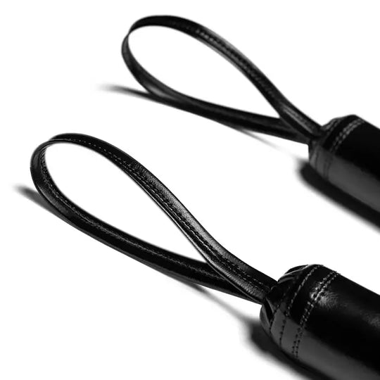 Close-up van twee zwarte handgreep lussen met fijne stiksels, onderdeel van trainingssticks, gefotografeerd op een witte achtergrond.