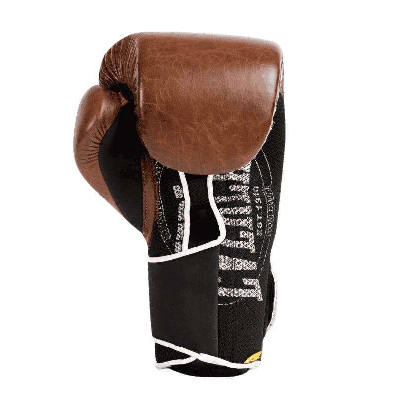 Afbeelding van de zijkant van een bruine Everlast 1910 Classic Training bokshandschoen. De handschoen heeft een leren buitenkant en een zwarte binnenkant met witte stiksels en een gedetailleerd Everlast-logo. De polsband is voorzien van een zwarte klittenbandsluiting met witte afwerking, wat zorgt voor extra ondersteuning en een vintage uitstraling.