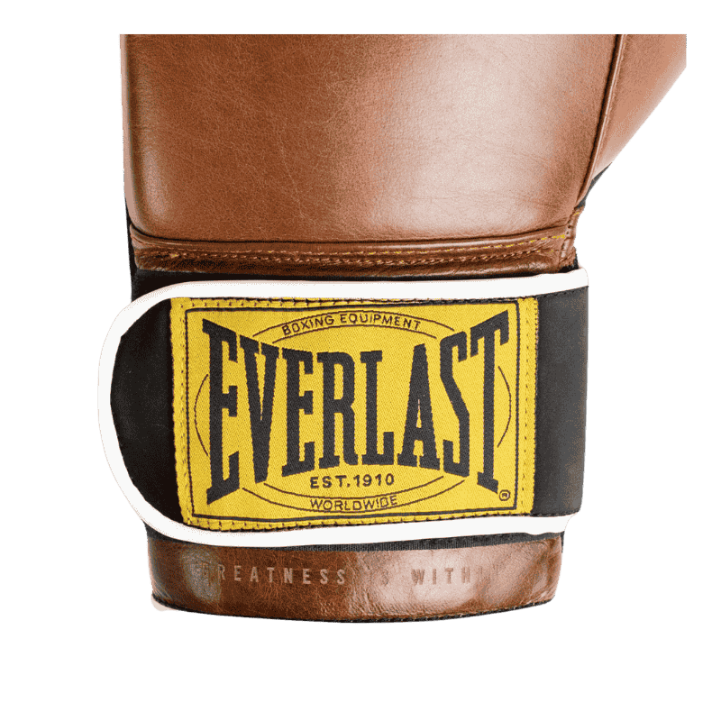 Close-up afbeelding van de polsband van een bruine Everlast 1910 Classic Training bokshandschoen. De polsband heeft een geel Everlast-logo met zwarte letters, omrand door een witte rand. Dit vintage ontwerp benadrukt de klassieke uitstraling van de handschoen, met de tekst 'Boxing Equipment Est. 1910 Worldwide' in het logo.