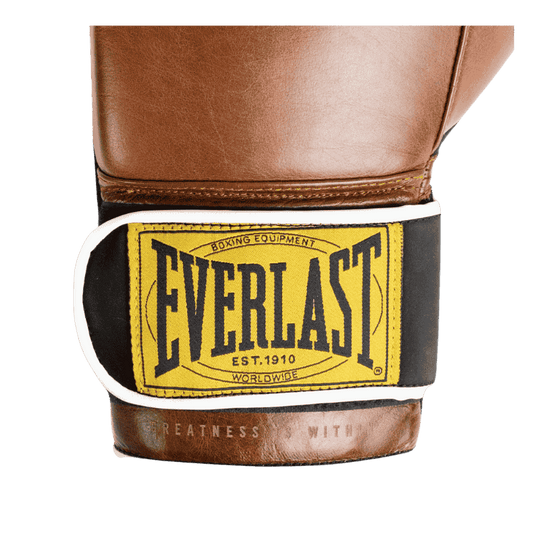 Close-up afbeelding van de polsband van een bruine Everlast 1910 Classic Training bokshandschoen. De polsband heeft een geel Everlast-logo met zwarte letters, omrand door een witte rand. Dit vintage ontwerp benadrukt de klassieke uitstraling van de handschoen, met de tekst 'Boxing Equipment Est. 1910 Worldwide' in het logo.