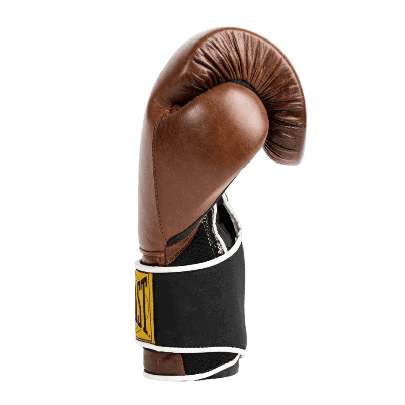 Afbeelding van de zijkant van een bruine Everlast 1910 Classic Training bokshandschoen, met de duim goed zichtbaar. De handschoen heeft een klassieke leren buitenkant en een zwarte polsband met het gele Everlast-logo en witte randafwerking. Het ontwerp combineert een vintage uitstraling met moderne ondersteuning en comfort voor de drager.