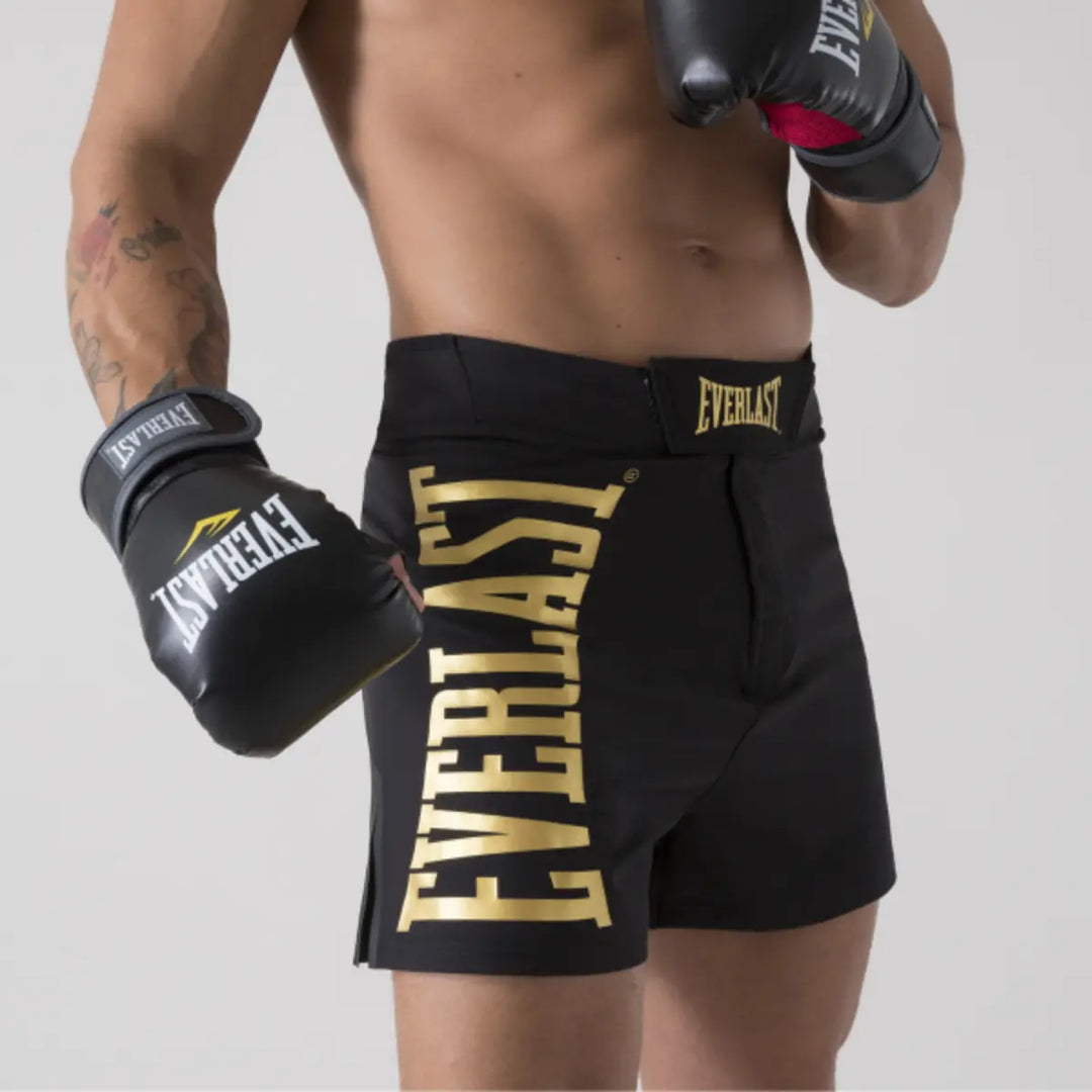 Sporter draagt zwart Everlast MMA broekje met goudkleurige Everlast logo-opdruk, gecombineerd met zwarte Everlast bokshandschoenen.