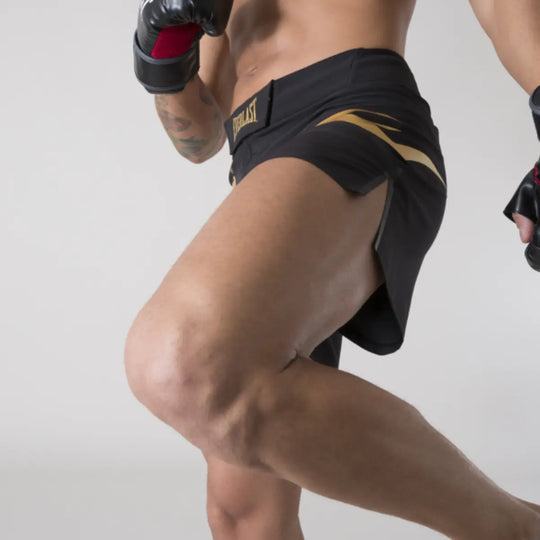 Close-up van een sporter in actie met zwart Everlast MMA broekje met goudkleurige details en hoge split voor bewegingsvrijheid.