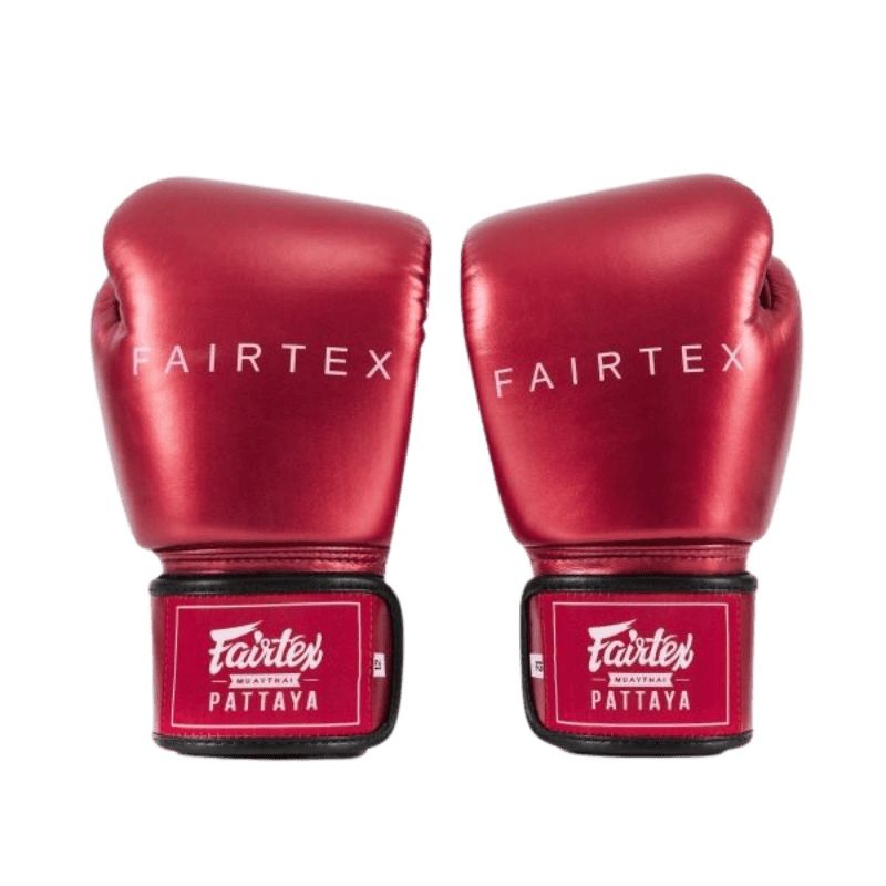 Een paar glanzend rode Fairtex bokshandschoenen, met het merklogo "Fairtex" op de knokkels en een rood klittenbandsluiting met het opschrift "Fairtex Muay Thai Pattaya".