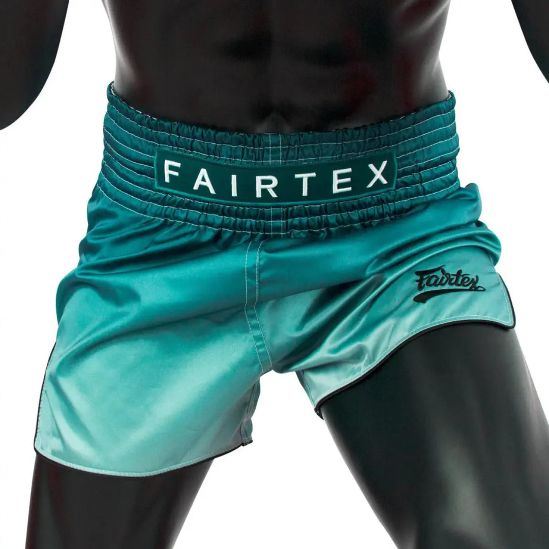 Close-up van een mannelijke sportman die een turquoise Fairtex kickboks broekje draagt, met elastische tailleband en Fairtex-logo zichtbaar op de voorkant.