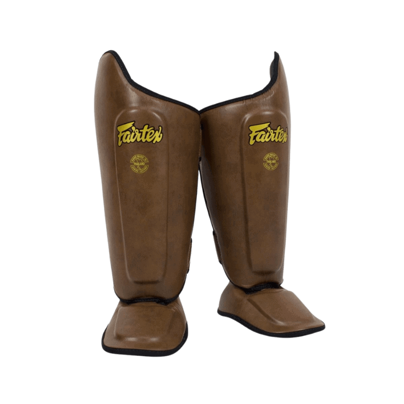 Een paar staande bruine scheenbeschermers met Fairtex-logo in goudkleurige letters.