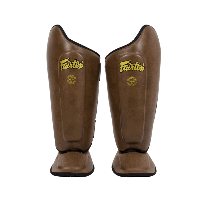 Een voorzijde weergave van bruine Fairtex scheenbeschermers staand tegen een donkere achtergrond.