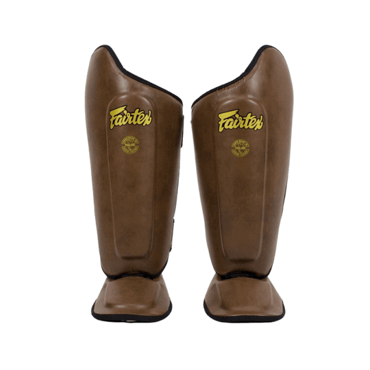 Een voorzijde weergave van bruine Fairtex scheenbeschermers staand tegen een donkere achtergrond.