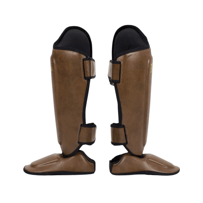 De achterkant van bruine Fairtex scheenbeschermers met zwarte bandjes en gouden logo.