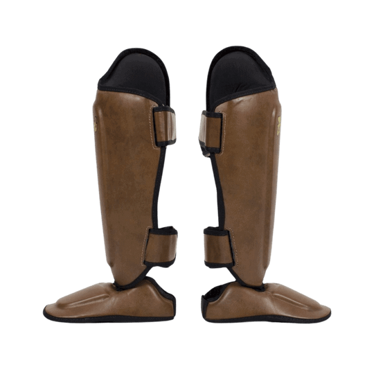 De achterkant van bruine Fairtex scheenbeschermers met zwarte bandjes en gouden logo.