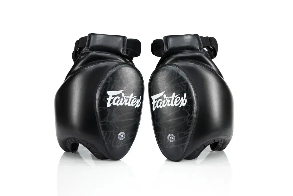 Twee Fairtex Buikbeschermers Zwart, gemaakt van duurzaam leer met witte Fairtex-logo’s op de voorzijde. De padding biedt maximale bescherming bij trap- en stoottraining, met een ergonomisch ontwerp dat de buik en ribben volledig bedekt.