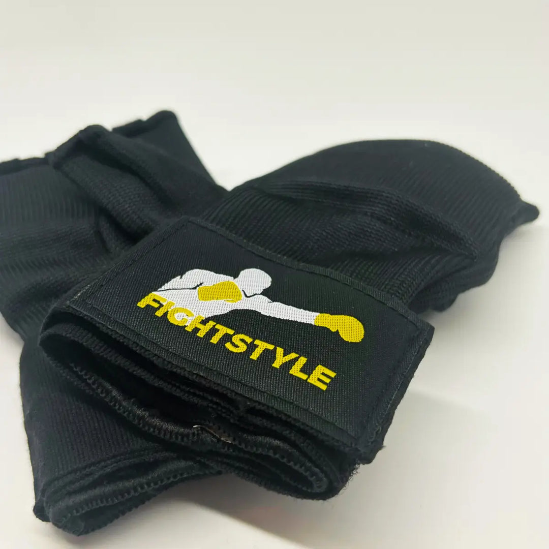 Zwarte Fightstyle binnenhandschoenen opgevouwen met opvallend logo van bokser met gele handschoenen op het polsstuk.