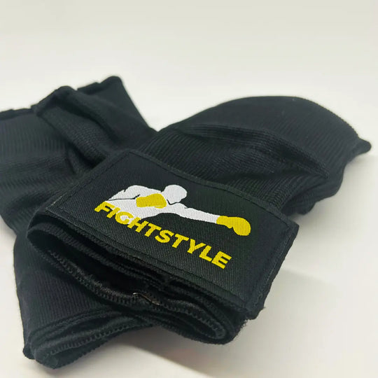 Zwarte Fightstyle binnenhandschoenen opgevouwen met opvallend logo van bokser met gele handschoenen op het polsstuk.