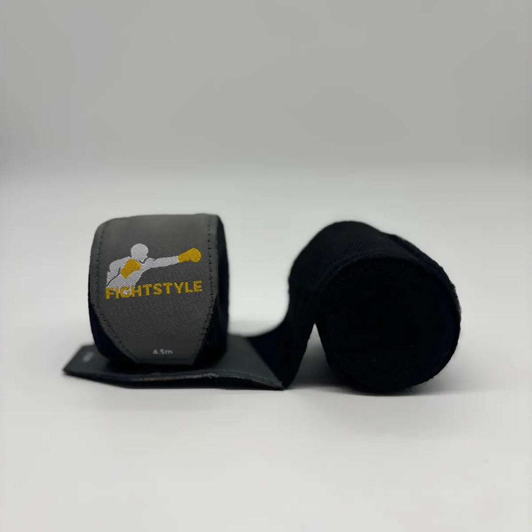 Zwarte Fightstyle bandages van 4.5 meter, deels uitgerold met zichtbaar logo, ideaal voor pols- en knokkelondersteuning tijdens bokstraining.
