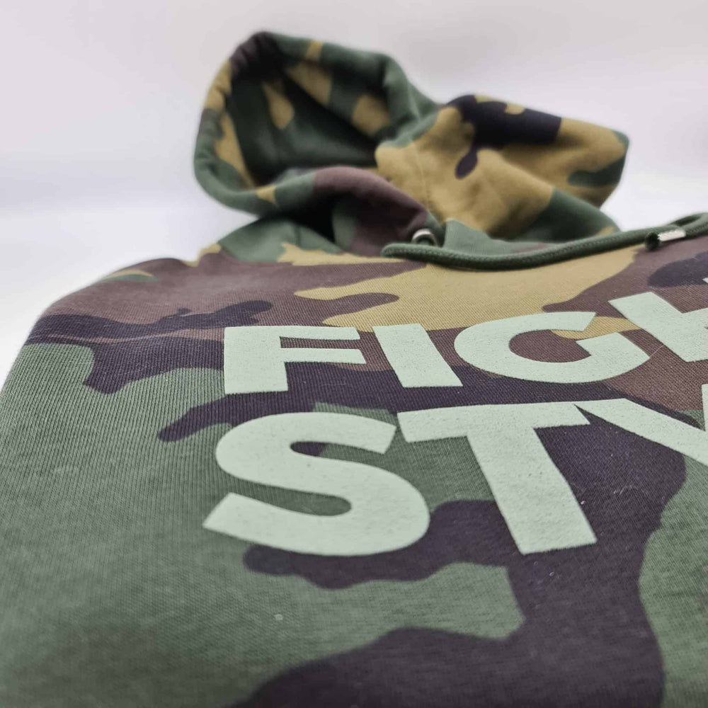 Close-up van de Fightstyle hoodie in camouflageprint, waarbij het logo duidelijk zichtbaar is op de borst. De zachte katoenen stof en subtiele textuur benadrukken de premium afwerking en streetwear-uitstraling van de hoodie.