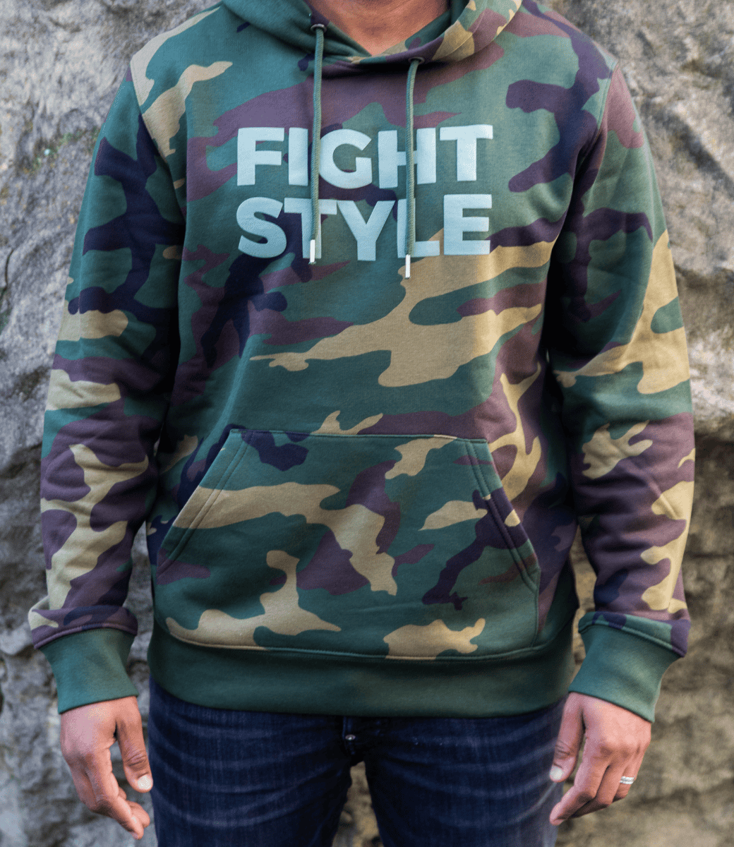 Close-up van de Fightstyle hoodie in camouflagegroen, gedragen door een model met jeans. De hoodie heeft een militair design, een zacht fleece-interieur en het herkenbare Fightstyle-logo op de borst — een statement piece voor fighters met stijl.