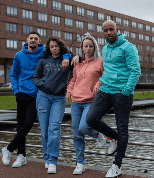 Vier modellen dragen de Fightstyle hoodies in blauw, antraciet, koraal en teal tijdens een straatshoot. De hoodies hebben een moderne pasvorm en een strak logo, ideaal voor een casual, sportieve streetstyle.