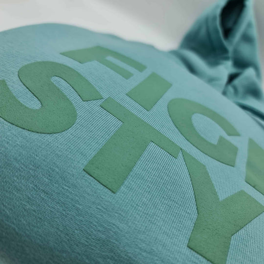Close-up van het verhoogde Fightstyle-logo op de Teal Monstera hoodie. De zachte textuur en matte afwerking benadrukken de premium kwaliteit en stijlvolle afwerking van deze streetwear essential.
